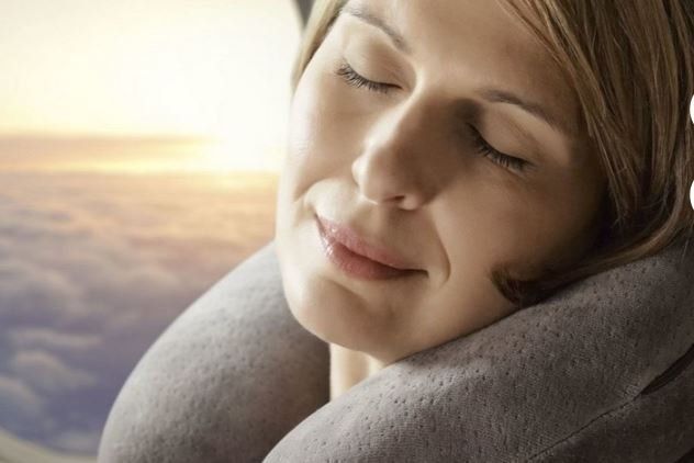 Primo piano di una persona sorridente che riposa avvolta in una coperta grigia, illuminata da una luminosa alba sul mare.