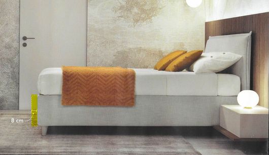 Camera da letto moderna con letto bianco, coperta arancione, arredamento neutro e lampada da comodino accesa.