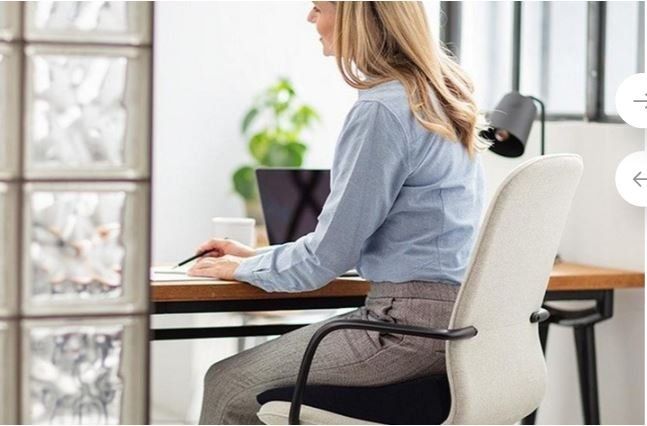 Persona al lavoro alla scrivania in un luminoso ufficio domestico, seduta su una sedia bianca accanto a un computer portatile.