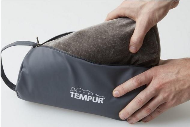 Delle mani comprimono un cuscino TEMPUR grigio in una borsa da trasporto grigia su sfondo bianco.