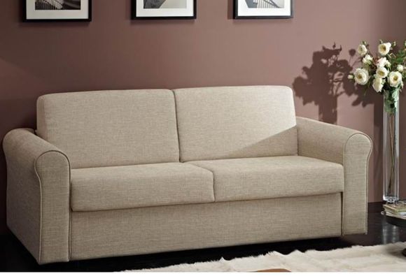 Divanetto beige in un soggiorno con parete marrone, quadri incorniciati e fiori su un tavolino.