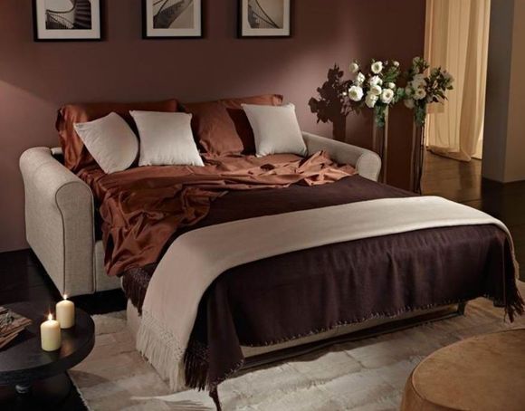 Accogliente camera da letto con letto ben rifatto, lenzuola marroni, quadri incorniciati e fiori vicino alla finestra.