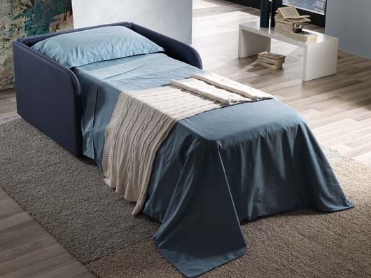 Divano letto imbottito blu con lenzuola e coperta in una stanza moderna accanto a una scrivania.