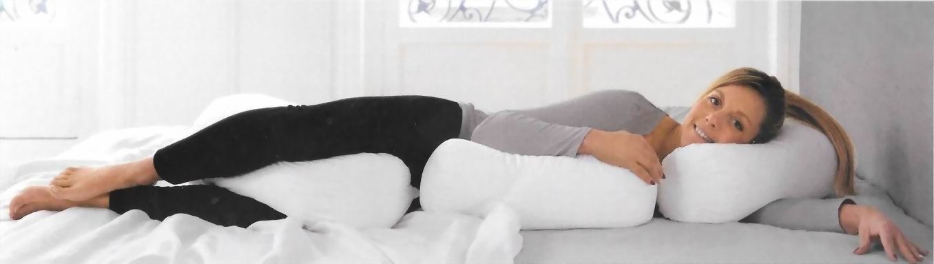 Una donna sdraiata su un letto bianco esegue un esercizio per le gambe in posizione laterale, indossando pantaloni neri e una maglietta grigia.