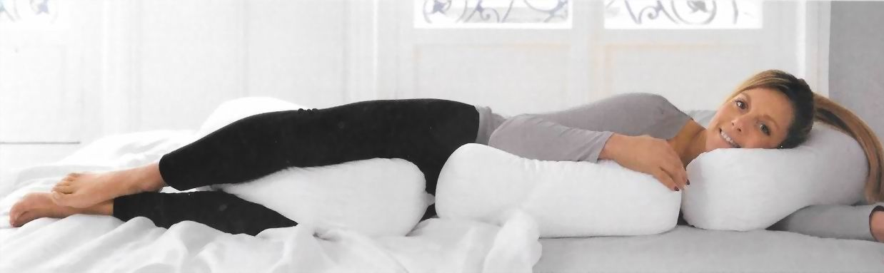 Una donna sdraiata su un letto bianco esegue un esercizio per le gambe in posizione laterale, indossando pantaloni neri e una maglietta grigia.