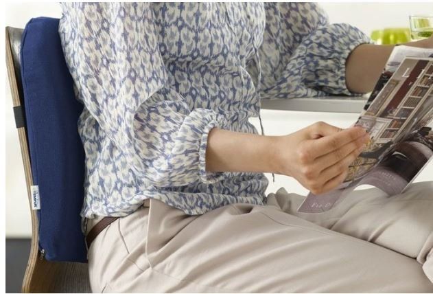 Persona seduta su un divano che legge una rivista, indossa una camicia blu a fantasia e pantaloni beige.