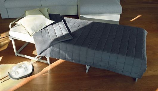 Una poltrona blu scuro con poggiapiedi in una stanza moderna e luminosa, con la luce del sole che illumina il pavimento in legno.