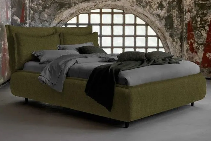 Letto imbottito color verde oliva con lenzuola grigie in una stanza rustica con finestra ad arco.