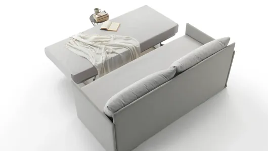 Divano componibile grigio accanto a un lettino con coperta piegata e vassoio su sfondo bianco.