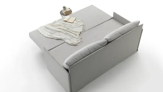 Divano imbottito grigio con coperta piegata e vassoio appoggiato sopra, mostrato su uno sfondo bianco minimalista.
