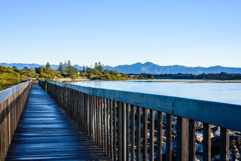 A Wooden Walkway Leading to A Lake with Mountains in The Background — Cemak Constructions in Urunga, NSW