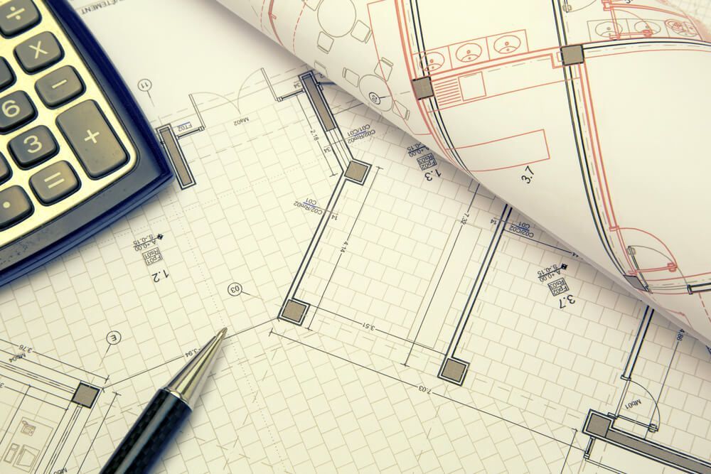A Calculator is Sitting on Top of a Blueprint Next to a Pen — Cemak Constructions in Coffs Harbour, NSW