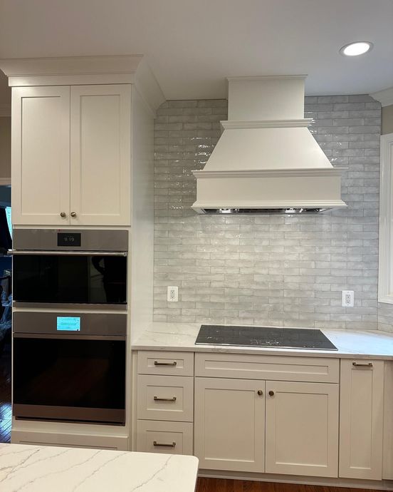 Modern kitchen with white cabinets, gray tile backsplash, built-in oven, and white range hood over a cooktop