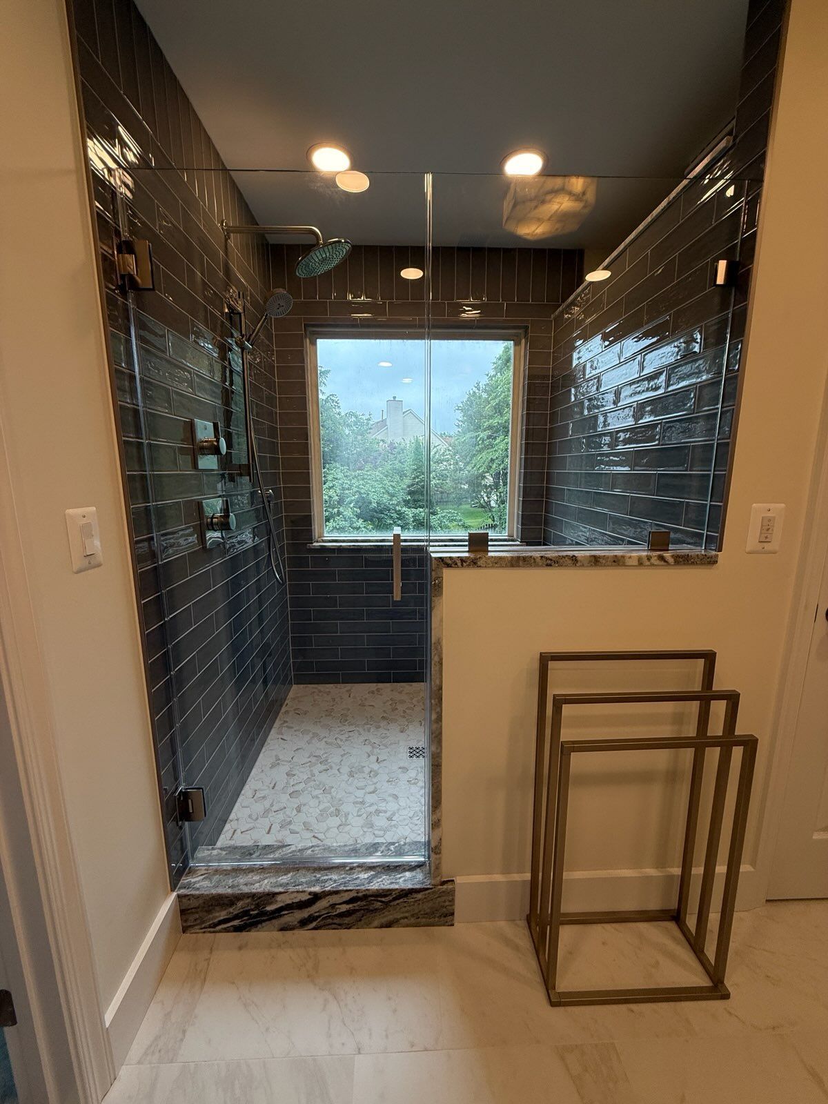 Narrow hallway under construction with dark tile walls, ceiling lights, a window, and stacked metal table frames.