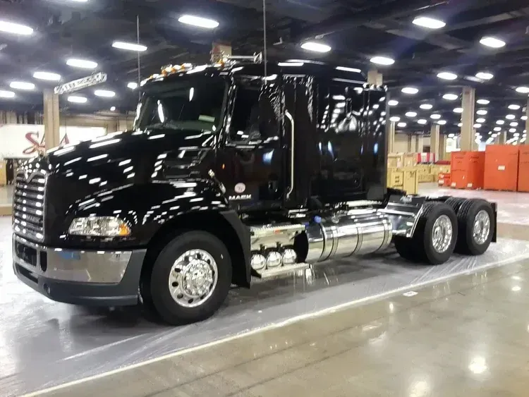 Black semi truck parked indoors at a convention center, shown in side view under bright lights