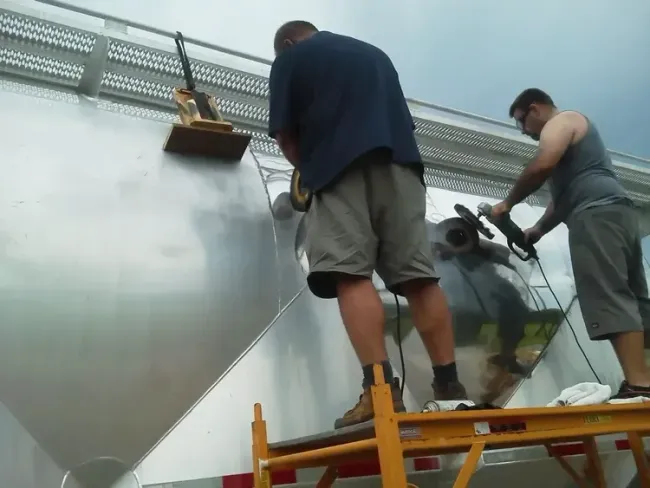 Two workers using a lift to clean a large metallic wall surface outdoors