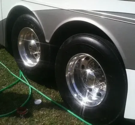 Close-up of a silver trailer’s two shiny wheels on grass, with a green hose nearby