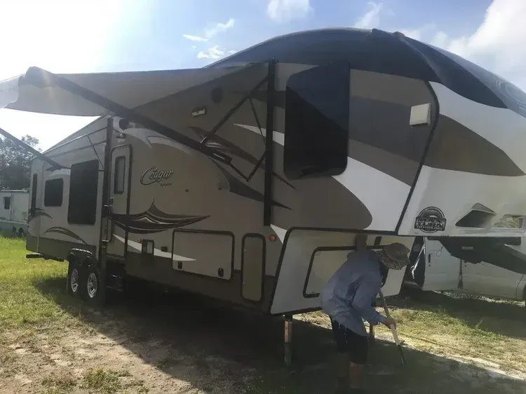 Large beige and gray fifth-wheel camper trailer parked on grass under a bright sky
