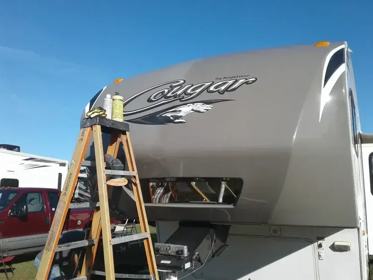 A gray RV with a ladder leaning against it under a clear blue sky