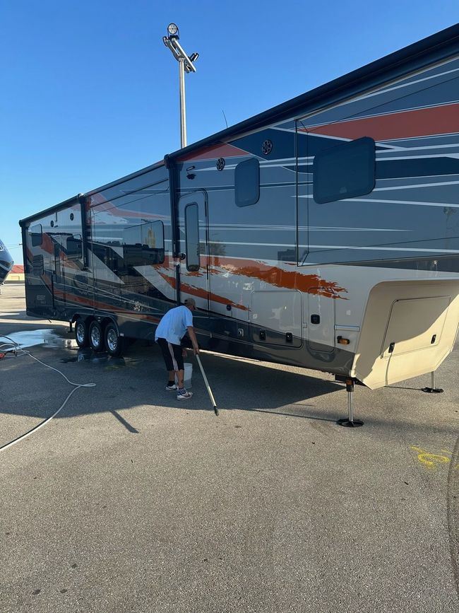 Person inspecting the side of a glossy black and white RV in a parking lot