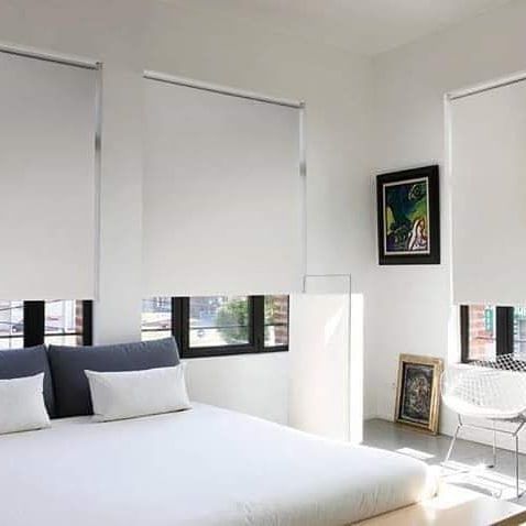 Dormitorio minimalista blanco con cama, ventanas con persianas y cuadros enmarcados en la pared.