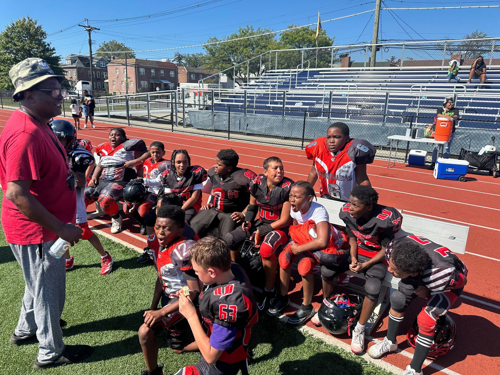 Football coach speaking to seated team on a field with empty bleachers in the background