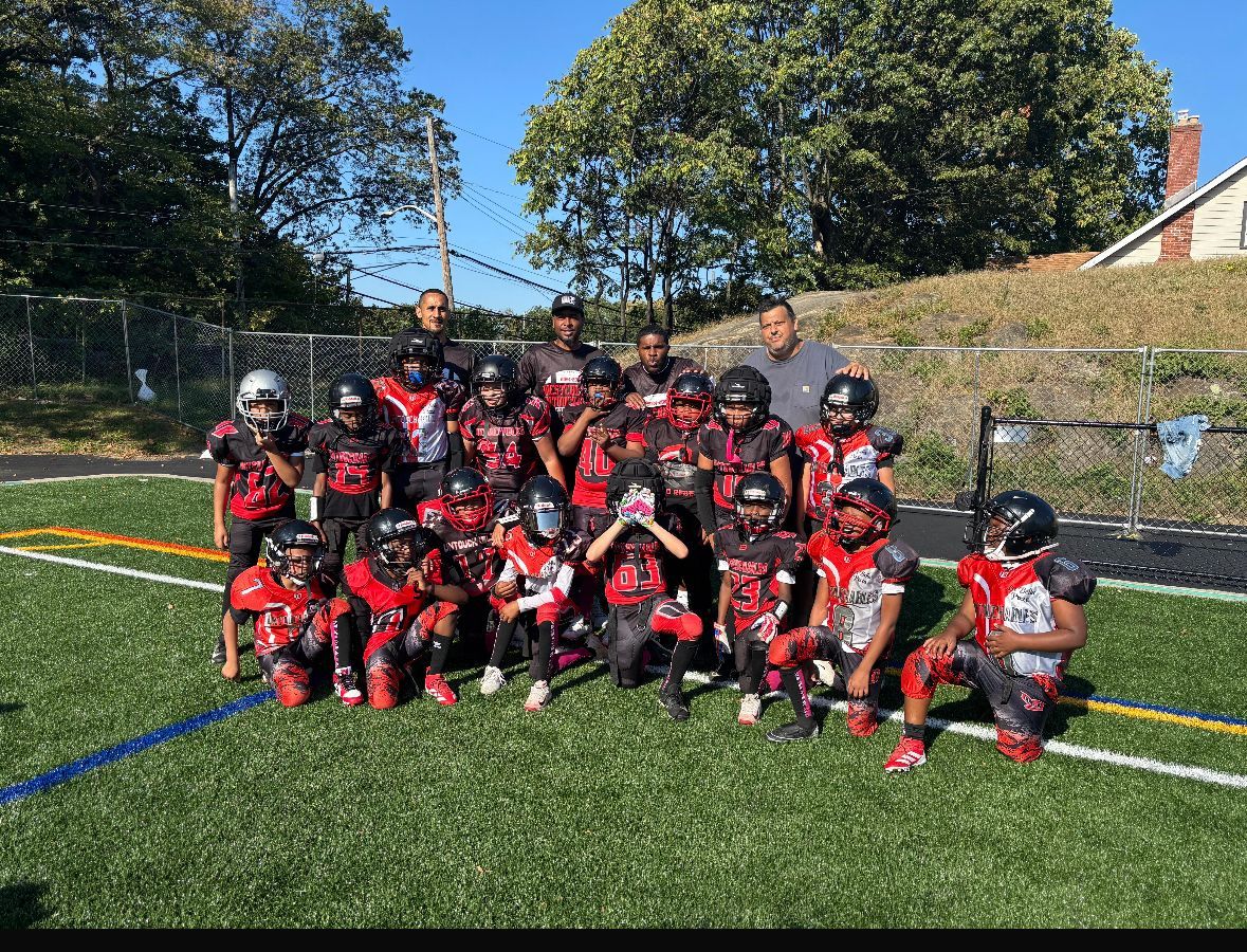 Youth footlball team in red and black uniforms posing on a grassy field under bright sun