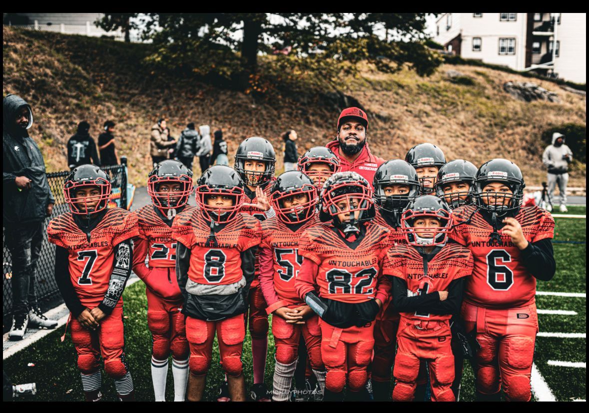 Black football helmet on a red jersey draped over a sideline bench on a football field