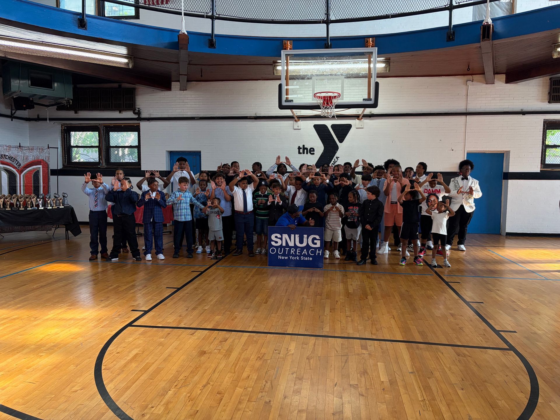 Group of people standing on a basketball court under a hoop, holding a blue SNUG banner in a gym