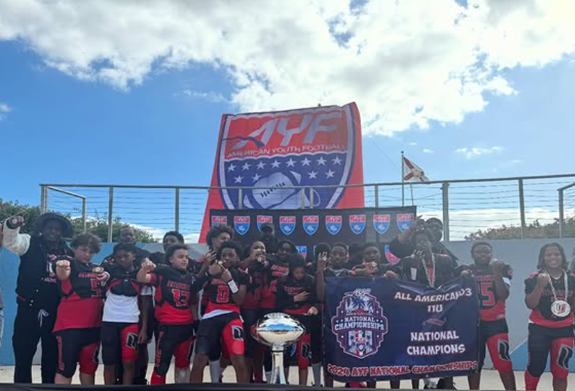 Youth cheer team posing with trophy and banner at an outdoor championship event under a bright sky