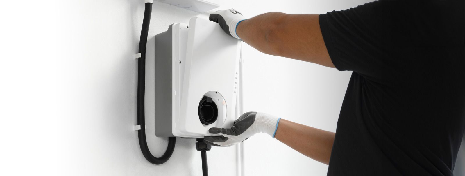 A man is installing an electric car charger on a wall.