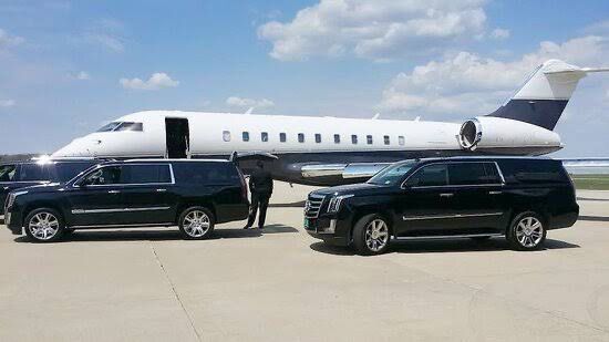 Black SUVs parked on tarmac in front of a private jet on a sunny day.