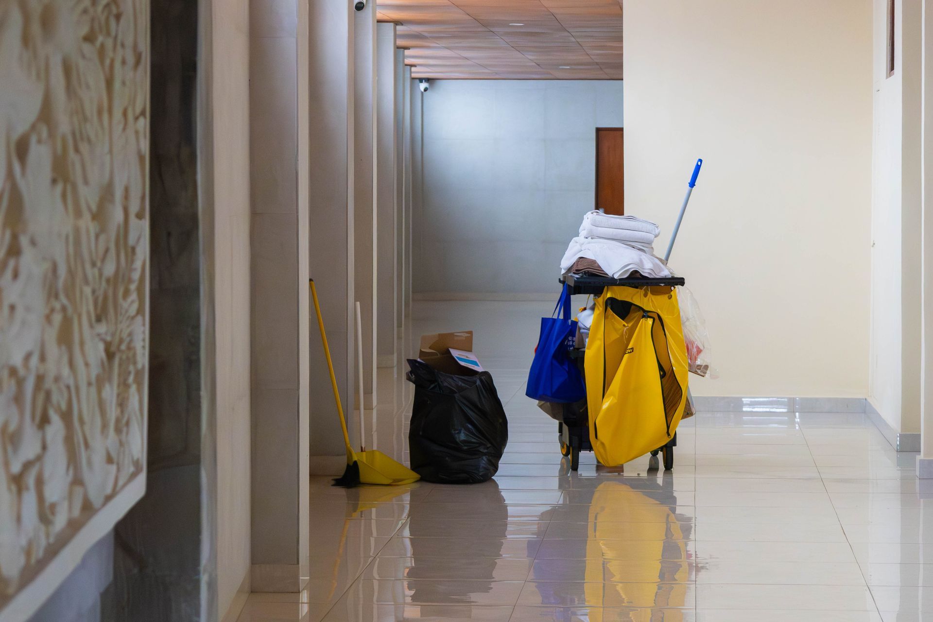 Yellow janitorial cleaning cart with mop and supplies in a tiled office hallway