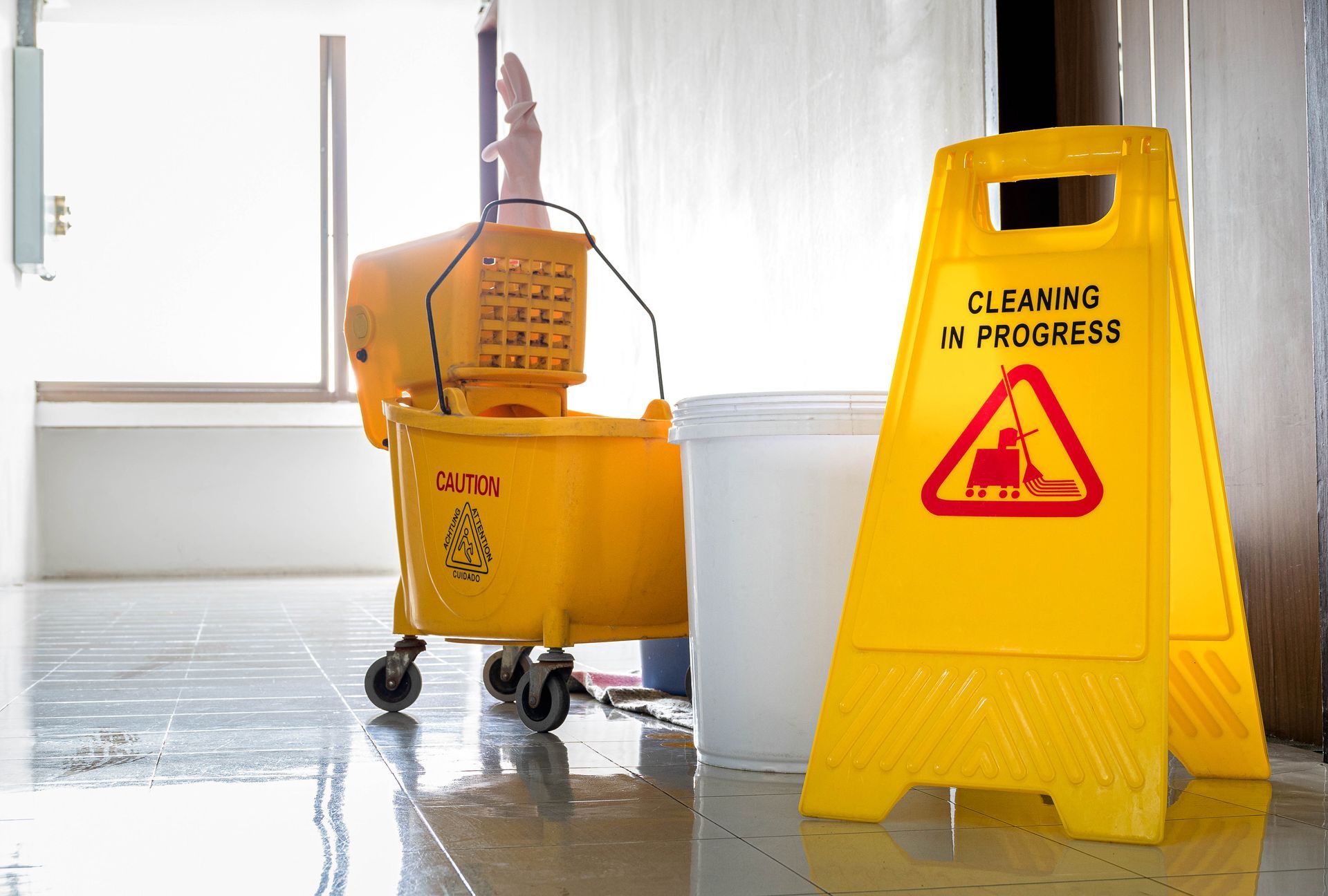 Yellow mop bucket and wringer next to a Cleaning in Progress caution sign in a hallway