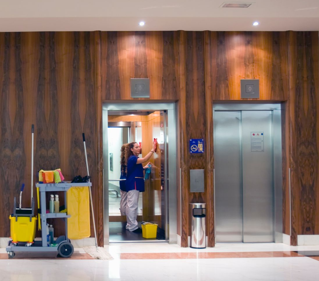 A person cleaning an elevator in a building, with cleaning supplies beside the elevator.