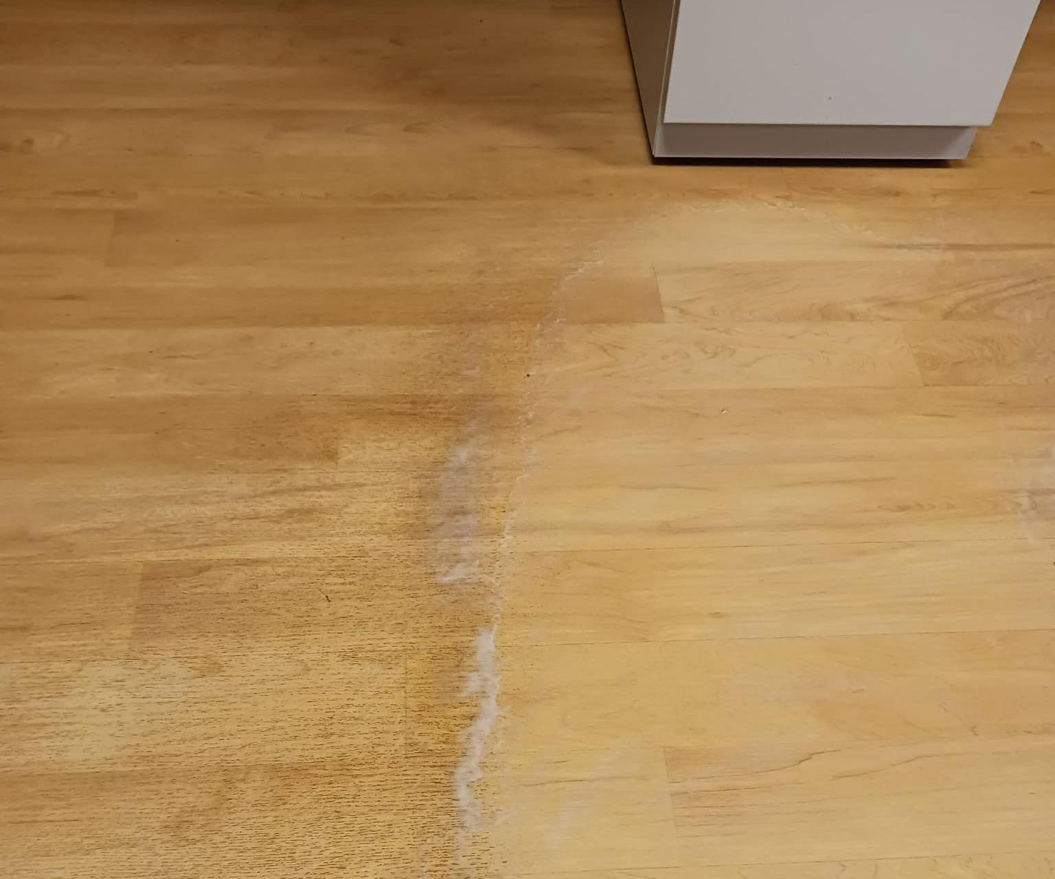 Wooden floor with a white cabinet leg in the corner, showing cleaning residue.