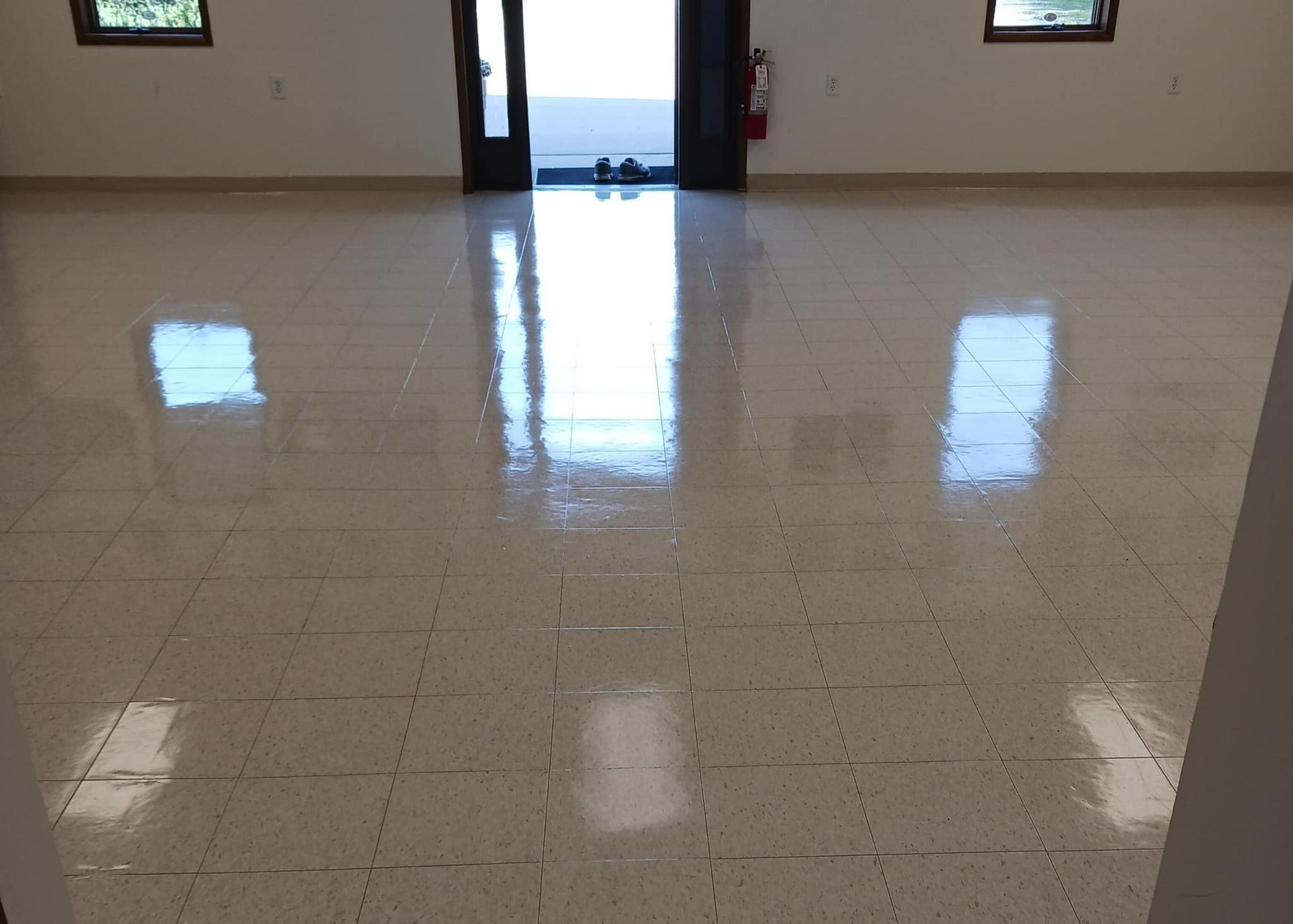 Empty room with shiny, light-colored tiled floor; windows and open double doors.