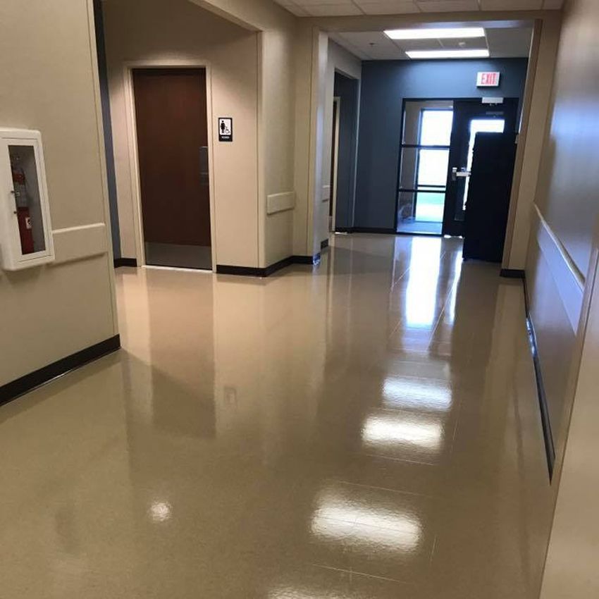 Hallway with shiny tan floor, beige walls, and brown door. A fire extinguisher and exit door are visible.
