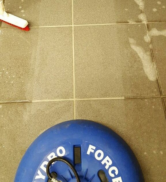 Blue Hydro Force floor cleaner on beige tile floor with white cleaning bubbles and a red and white scrubber.