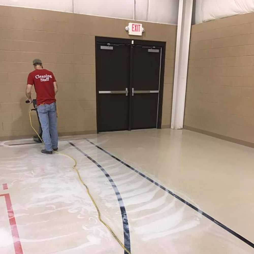 Man cleaning gym floor with floor scrubber near exit doors.
