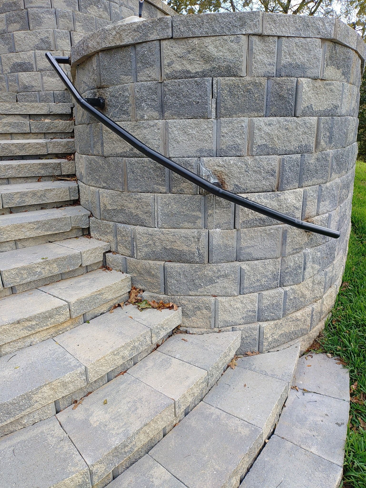 Curved stone stairway with a black handrail beside a gray stone wall outdoors