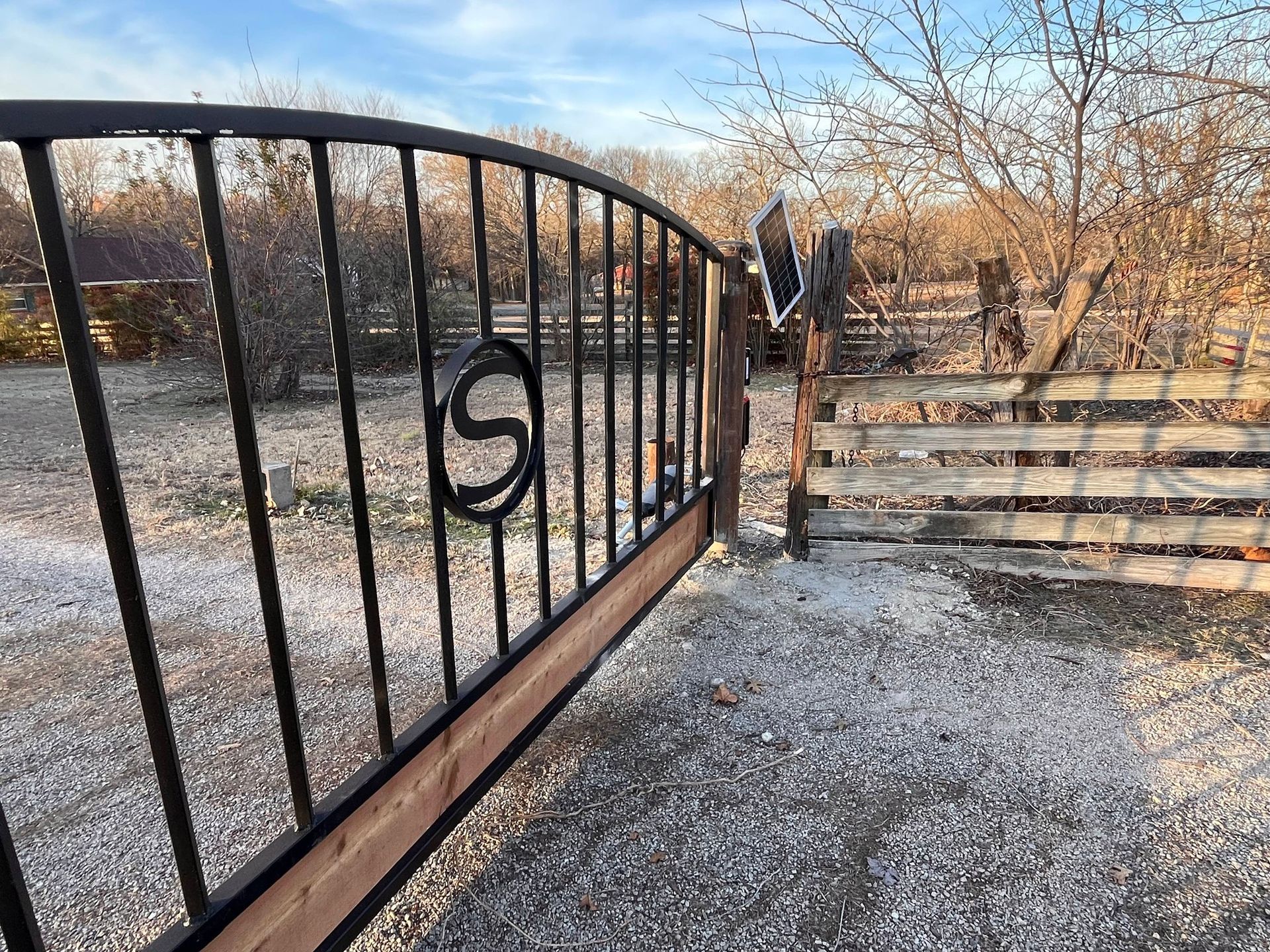 Black metal gate beside a gravel path and stone steps in a bare winter landscape