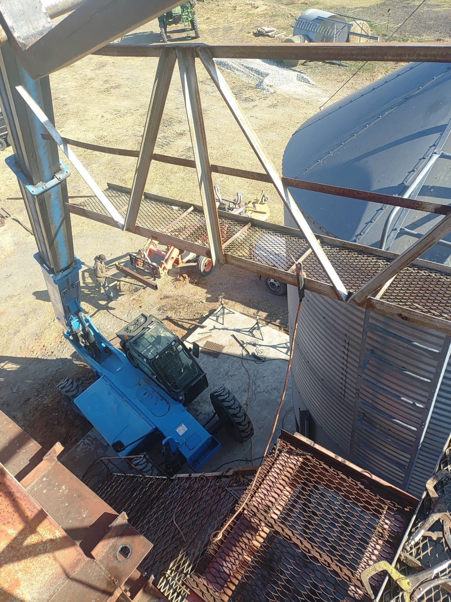 Blue construction machine beside a rusted metal structure and sandy ground at an industrial site