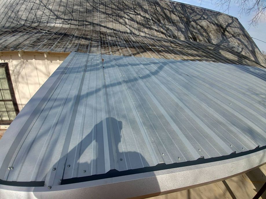 Blue-gray corrugated roof panel on a structure, with tree shadows and a person’s shadow in the foreground