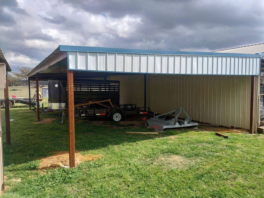 Carport with a blue metal roof and a parked vehicle beside a white shed on a grassy yard.