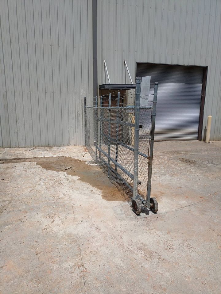 Wheeled wire cart with a metal top beside a gray corrugated wall and open doorway on gravel.