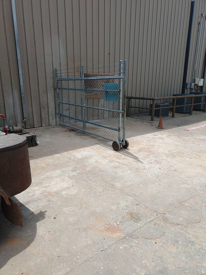 Blue metal cart on wheels in a dusty outdoor area beside a wall and planters