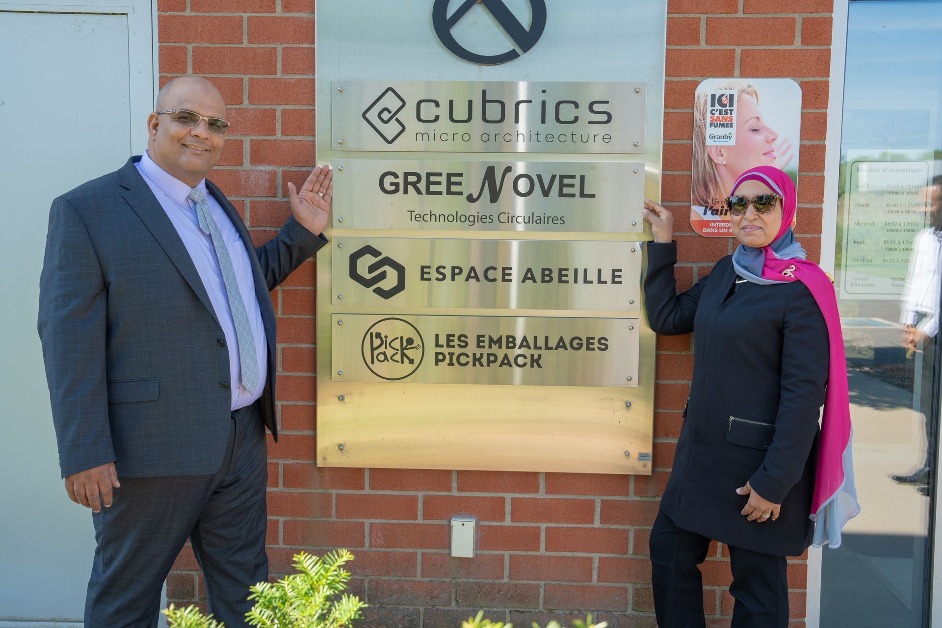 A man and a woman are standing in front of a brick building holding signs.