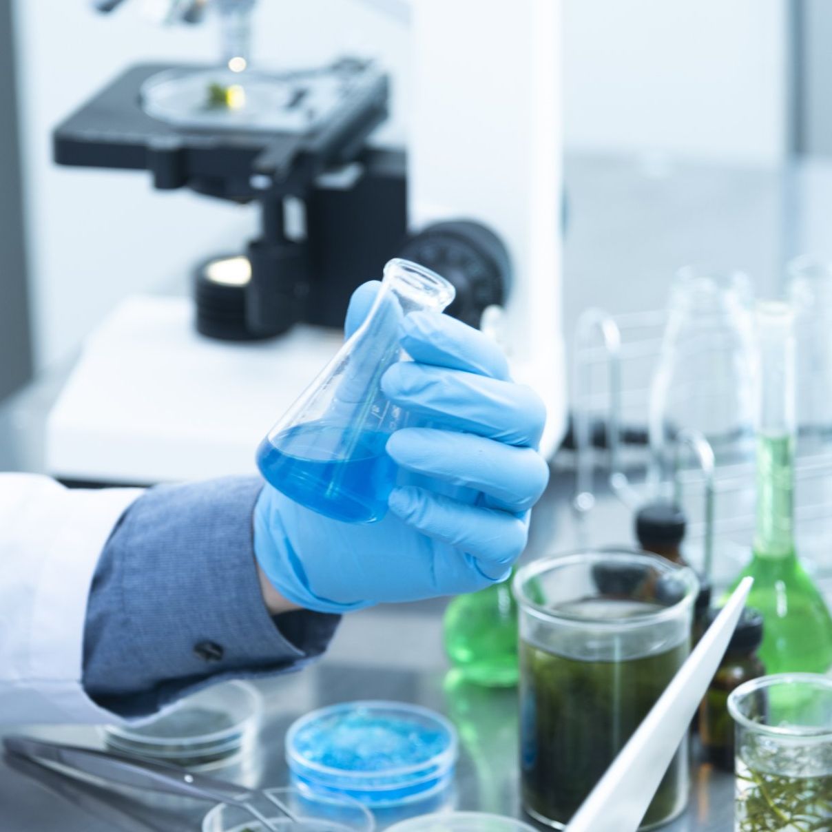 A person wearing blue gloves is holding a beaker of blue liquid