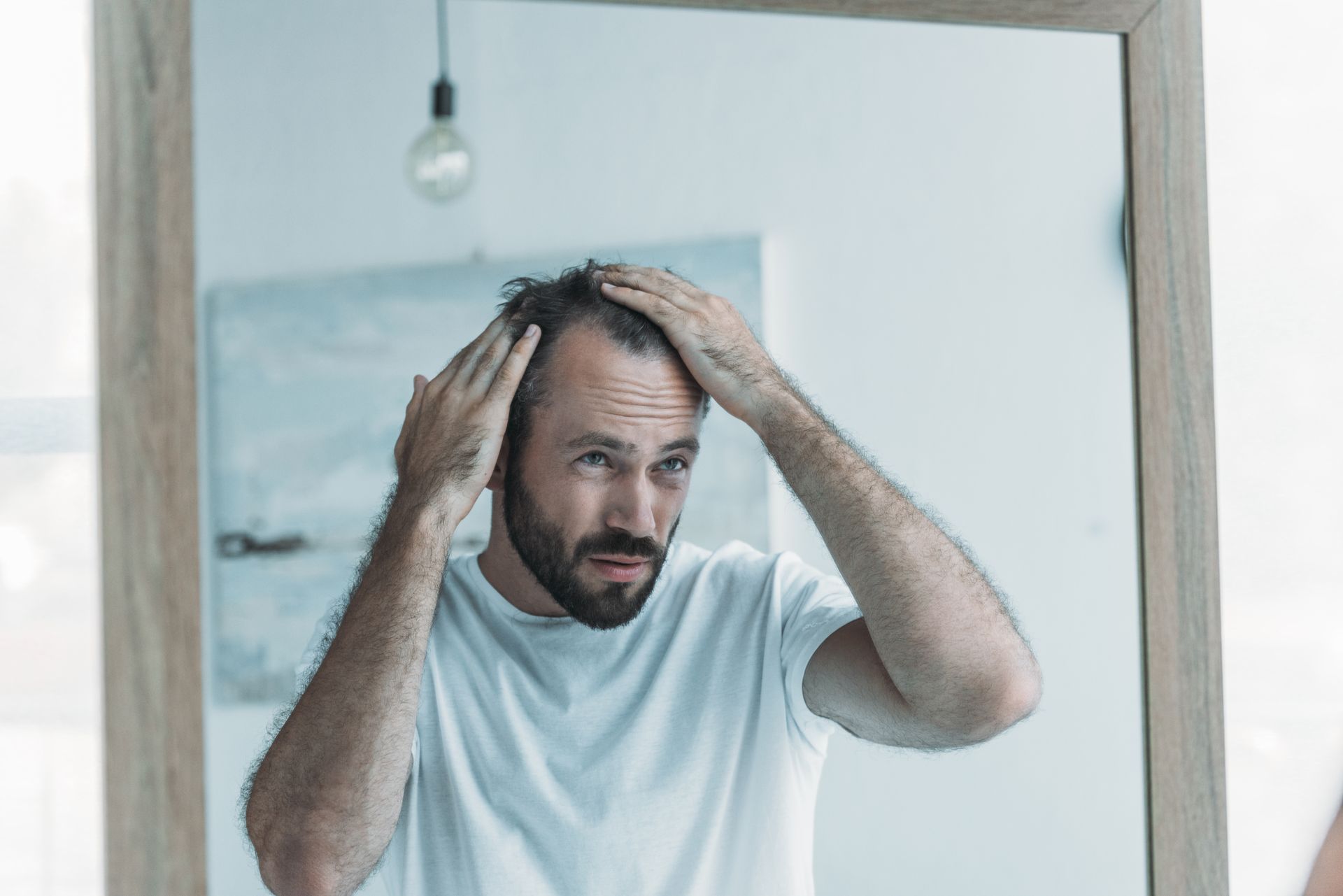 A man is looking at his hair in a mirror.